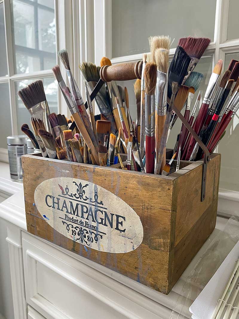 An old wooded box holds a variety of paint brushes.