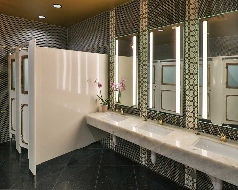 Opulent and elegant. The restrooms were not overlooked with detail and a curated selection of penny round, brass inlay ceramic tile borders, onyx counters and terrazzo flooring. Custom partitions by Slater Design Studios. Tile and Stone: Walker Zanger. Photo courtesy of Todd McBrayer/Breslin Builders